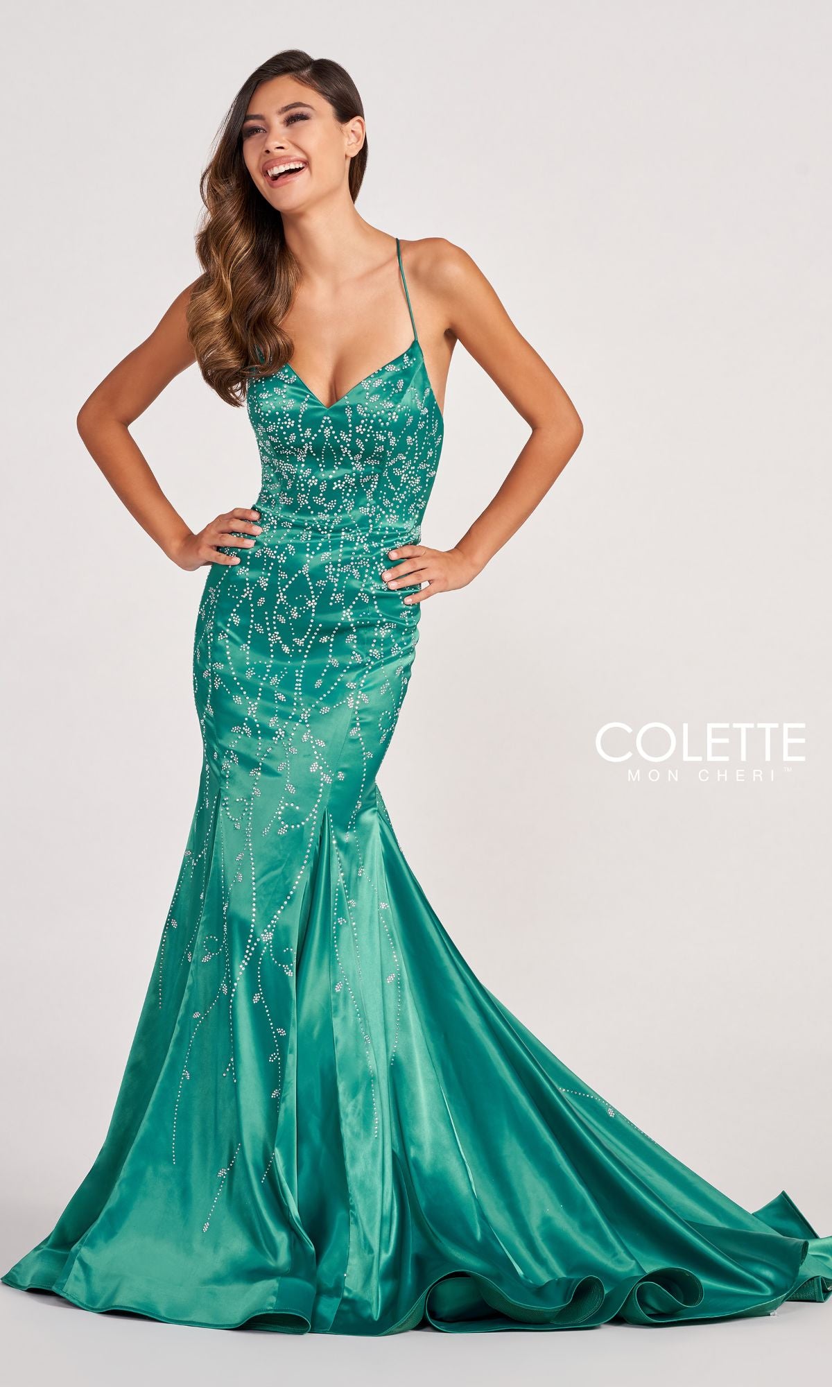 A woman poses in the Colette CL2043 Keyhole-Back Long Satin Prom Dress, a fitted mermaid gown with thin straps, sparkling green embellishments, a flared bottom, and a subtle train.